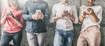 4 people standing in a row all looking at their cell phones