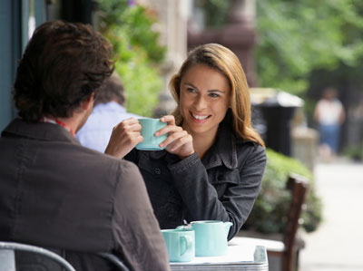 Woman on a date with a man, smiling at him and holding a blue coffee cup