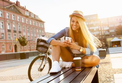 Smiling woman sitting on a bench in the sunshine texting on her cell phone