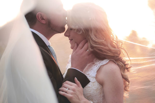 Upward vs Christian Mingle: Which Dating App Is Better? 1 New husband kissing his bride on the forehead with sunshine in the background